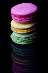 Multi-colored macaroons on a black background with reflection.