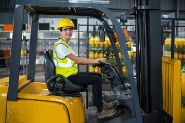 Portrait of smiling female factory worker driving forklift