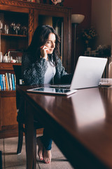 Entrepreneur calling on phone and working on line with a laptop sitting in a desk at home - business, technology, multitasking concept