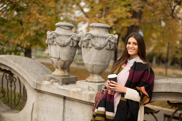 Fototapeta premium Woman standing outside, drinking coffee to go and holding a mobile phone in hand