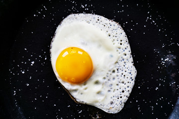 Closeup chips are down egg in a black cast-iron pan, without oil, sprinkled with salt. Concept health.