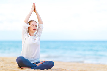 Fototapeta na wymiar woman practices yoga and meditates in lotus position on beach