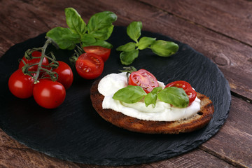 Fototapeta na wymiar Bread with cream cheese and tomato for lunch table. Sharing antipasti on party or summer picnic time over wooden rustic background.
