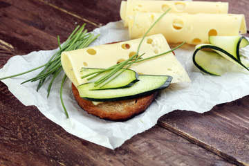 Bread with slices of cheese for lunch table. Sharing antipasti on party or summer picnic time over wooden rustic background.