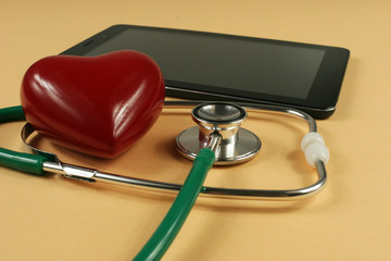 Stethoscope, tablet computer and heart on orange background.