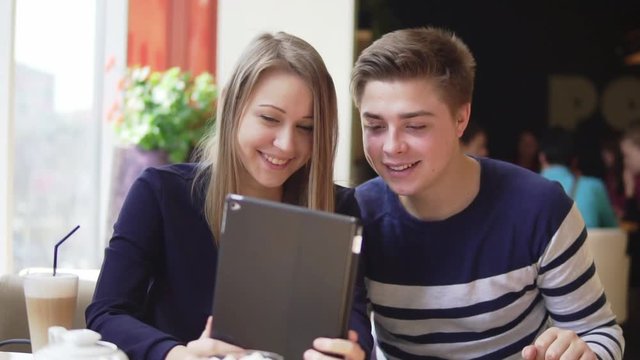 Young attractive couple using digital tablet computer, looking at the screen in cafe.