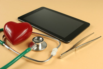 Stethoscope, tablet computer and heart on orange background.
