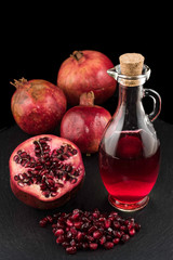 Pomegranates, seeds and bottle of juice on black plate with black background