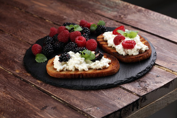 Bread with cheese cream and blackberries and raspberries for lunch table. Sharing antipasti on party or summer picnic time over wooden rustic background.
