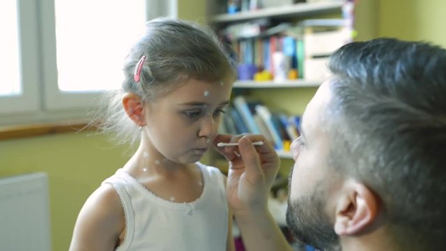 Little girl with chickenpox, father applying antiseptic cream to rash