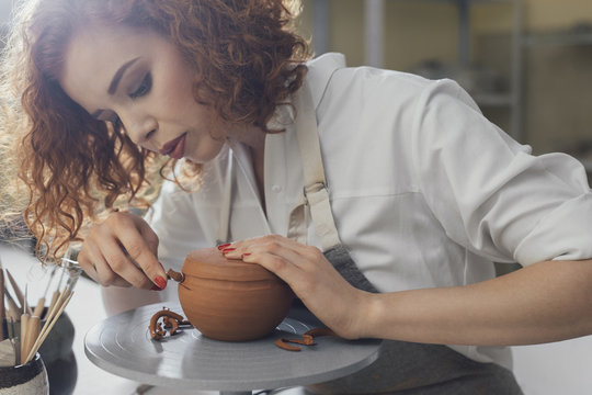 Female potter molding shape to clay with work tool at table