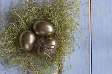 A decorative easter golden eggs  on a dry grass on a light wooden background