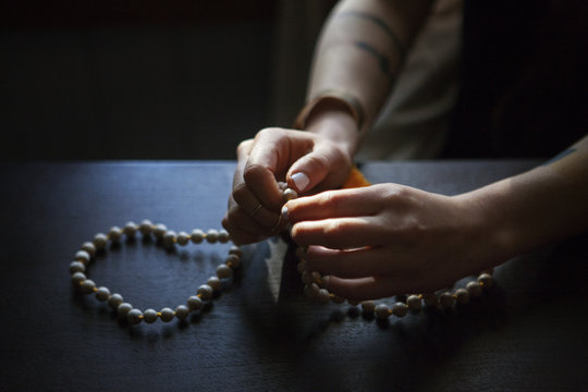 Cropped image of woman praying with beads in darkroom at home
