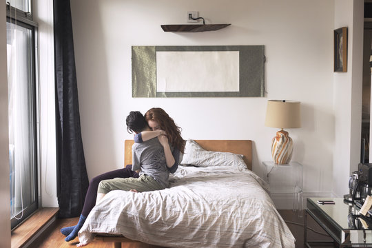 Lesbian couple embracing each other while sitting on bed at home