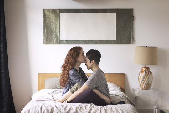 Romantic lesbian kissing on girlfriend's forehead while sitting on bed at home