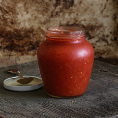 Tomato sauce in a transparent jar on a wooden surface