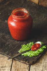 Tomato sauce in a spoon on lettuce leaves and in a transparent jar on a wooden surface