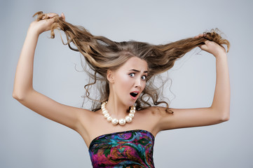 Haircare. Blonde woman holding her hair angry face expression gray background