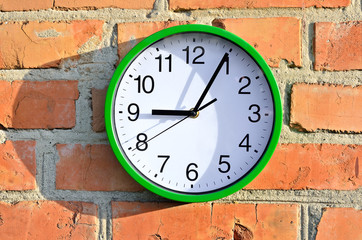 Fototapeta na wymiar Green wall clock hanging on a brick wall