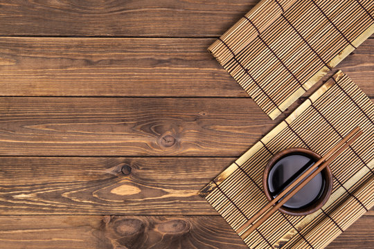 Background for sushi. Bamboo mat, soy sauce, chopsticks on wooden table. Top view with copy space