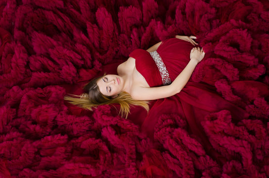 Pregnant young woman in a beautiful lush dress cloud royal burgundy. Lies on the floor