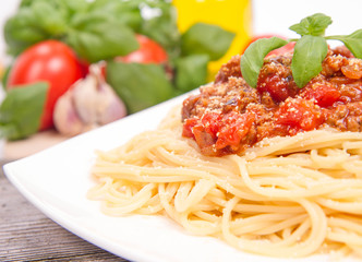 Spaghetti bolognese,some tomatoes, olive oil, basil, garlic, and raw pasta in the background