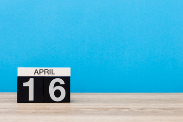 April 16th. Day 16 of month, calendar on wooden table and blue background. Spring time, empty space for text