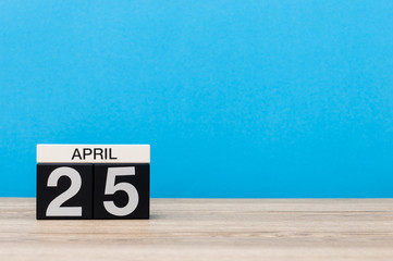 April 25th. Day 25 of month, calendar on wooden table and blue background. Spring time, empty space for text