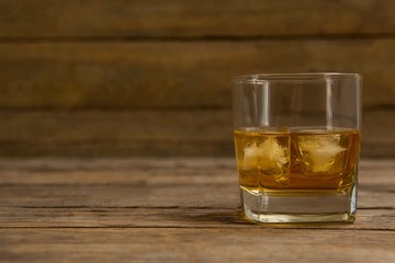 Glass of whisky with ice cube on wooden table