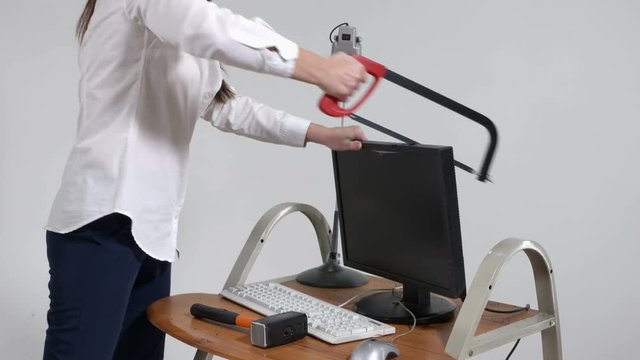 Crazy office worker destroying desktop computer with hacksaw and sledgehammer