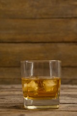Glass of whisky with ice cube on wooden table