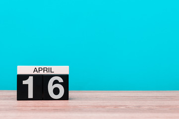 April 16th. Day 16 of month, calendar on wooden table and turquoise background. Spring time, empty space for text