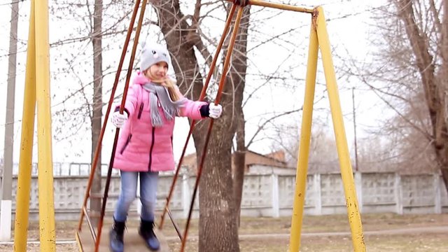 Little girl on swing in city park, happy child on swing. Concept girl in pink on a swing quickly.