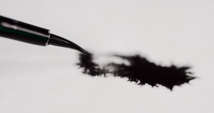 Macro shot of a thin paintbrush painting on paper with beautiful ink bleeds