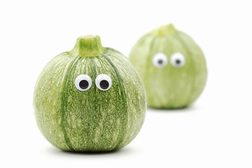 two round zucchini with googly eyes on white background - funny food