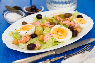 salad with salmon, eggs and olives on white dish