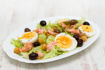 salad with salmon, eggs and olives on white dish