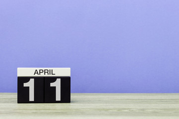 April 11th. Day 11 of month, calendar on wooden table and purple background. Spring time, empty space for text
