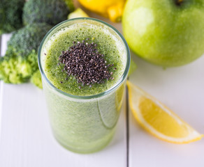 Broccoli smoothie in glass bowl on white wooden background with lemon and apple.