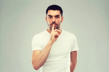 young man making hush sign over gray background