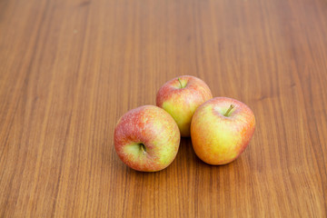 Drei gesunde rot-gelbe Äpfel auf Kirschbaum-Holztisch, Blick seitlich oben