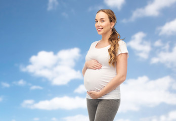 happy pregnant woman touching her belly over sky