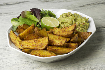 Spicy potato wedges with guacamole, green salad and lime