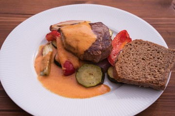 Beef steak served  with grilled vegetables consist from zucchini, shallot onion, red sweet pepper and spring onion. Sauce is made from cream and red pepper, served with slice of rustic brown bread. 