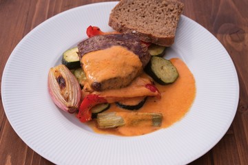 Beef steak served  with grilled vegetables consist from zucchini, shallot onion, red sweet pepper and spring onion. Sauce is made from cream and red pepper, served with slice of rustic brown bread. 
