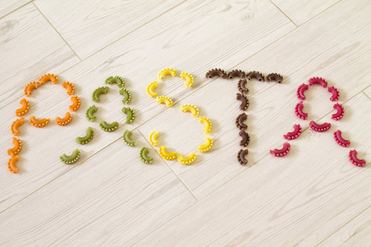 Written text "Pasta" from colorful raw pasta. (Beet, carrot, paprika, spinach, grape seed). 