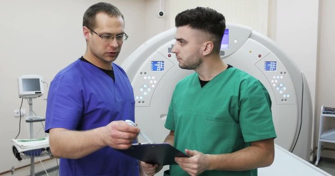 Two young doctors discussing the history of the patient on a background of a new magnetic resonance imaging.