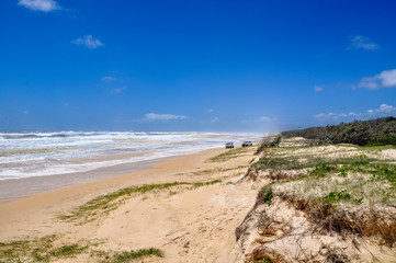Fototapeta na wymiar Stunning view of 75 Mile Beach on Fraser Island, Queensland, Australia, located in the Great Sandy National Park. Rough ocean on a sunny day, two four wheel drive cars in the background.