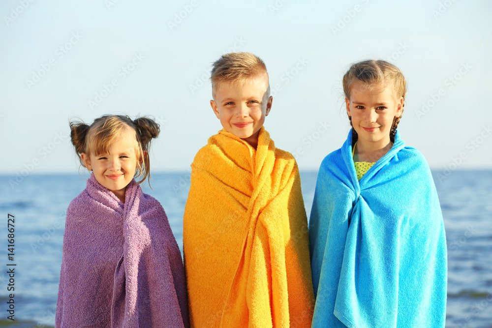 Wall mural cute kids wrapped in towel on beach