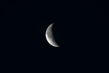 Closeup of the Moon in Waning Crescent Phase, showing detailed craters. Dark night background.